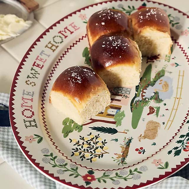 Three bread rolls on a decorative plate with a vintage design