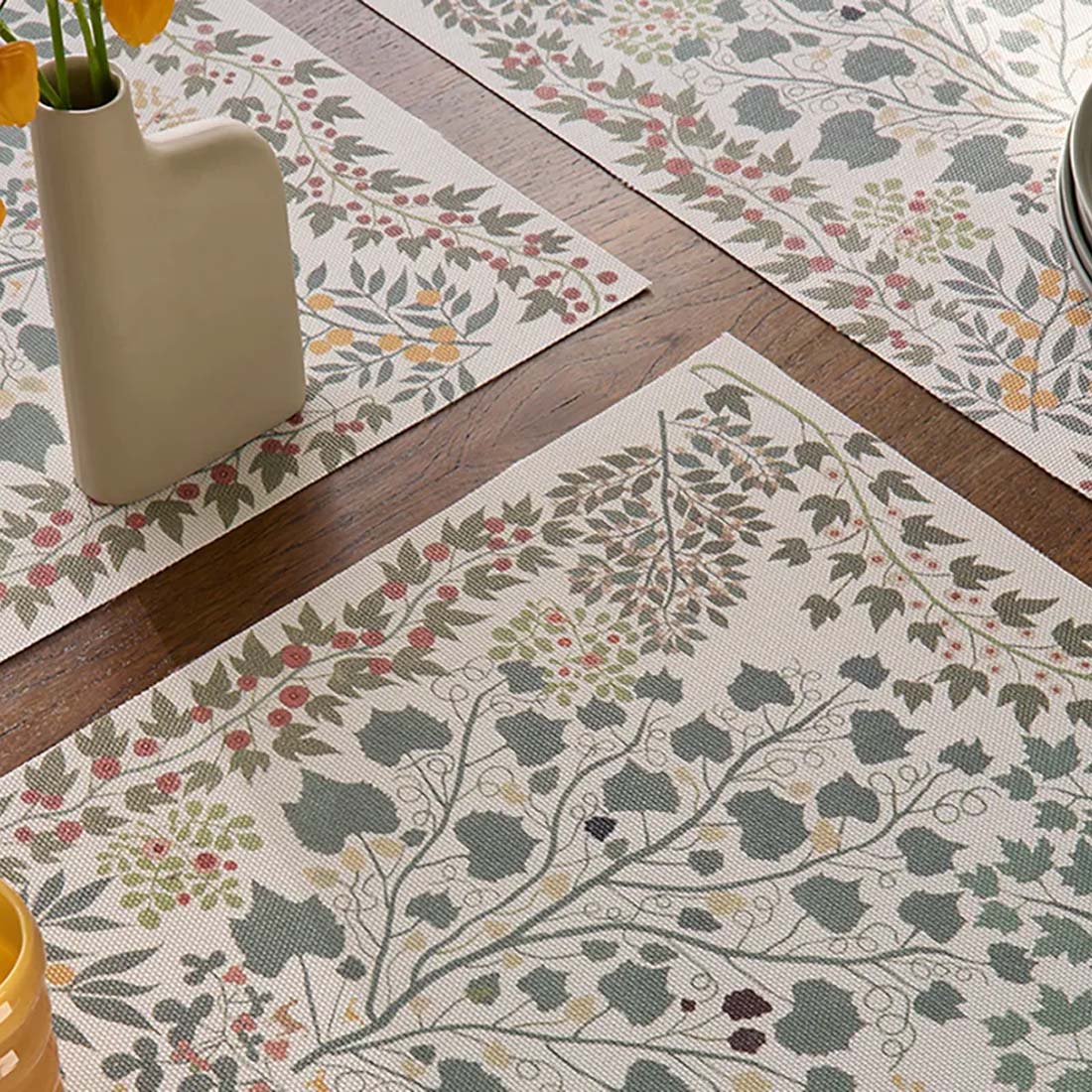 A woven textile placemat with a nature-inspired geometric pattern featuring branches and vines in a multicolor print.