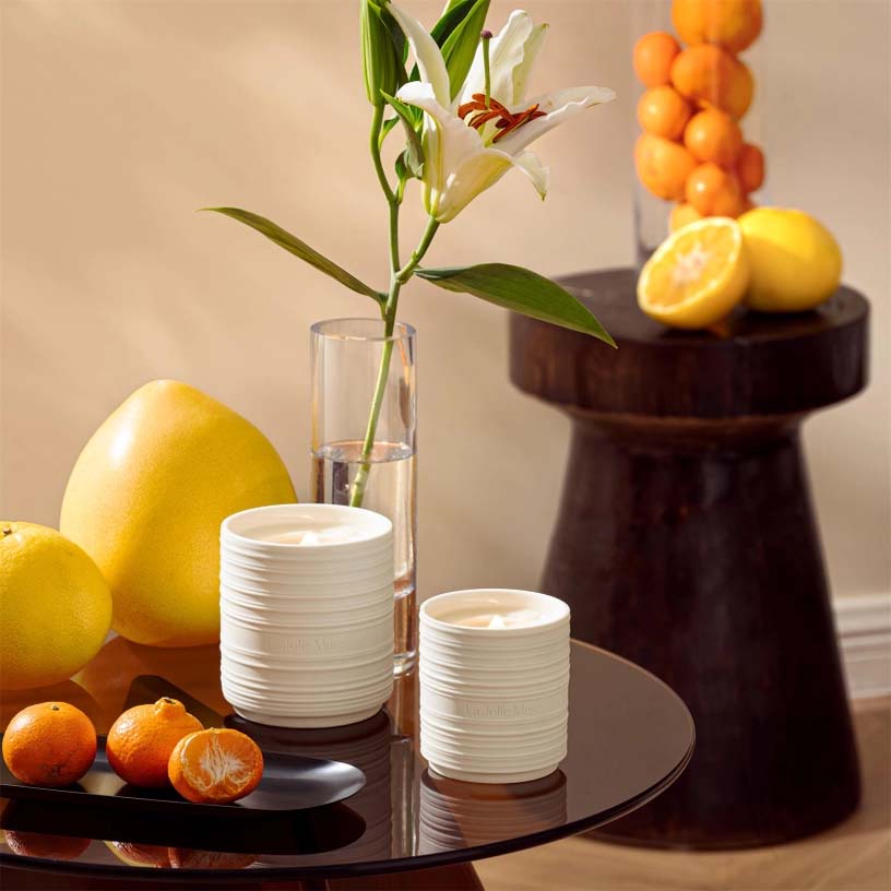 A white ceramic candle with a textured design, branded 'L'Joie Muse', with a lit wick and a warm base.