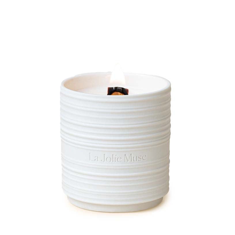 A white ceramic candle with a rippled design, branded with 'L'Occitane en Provence', with a lit wick and a cup of wax on top.