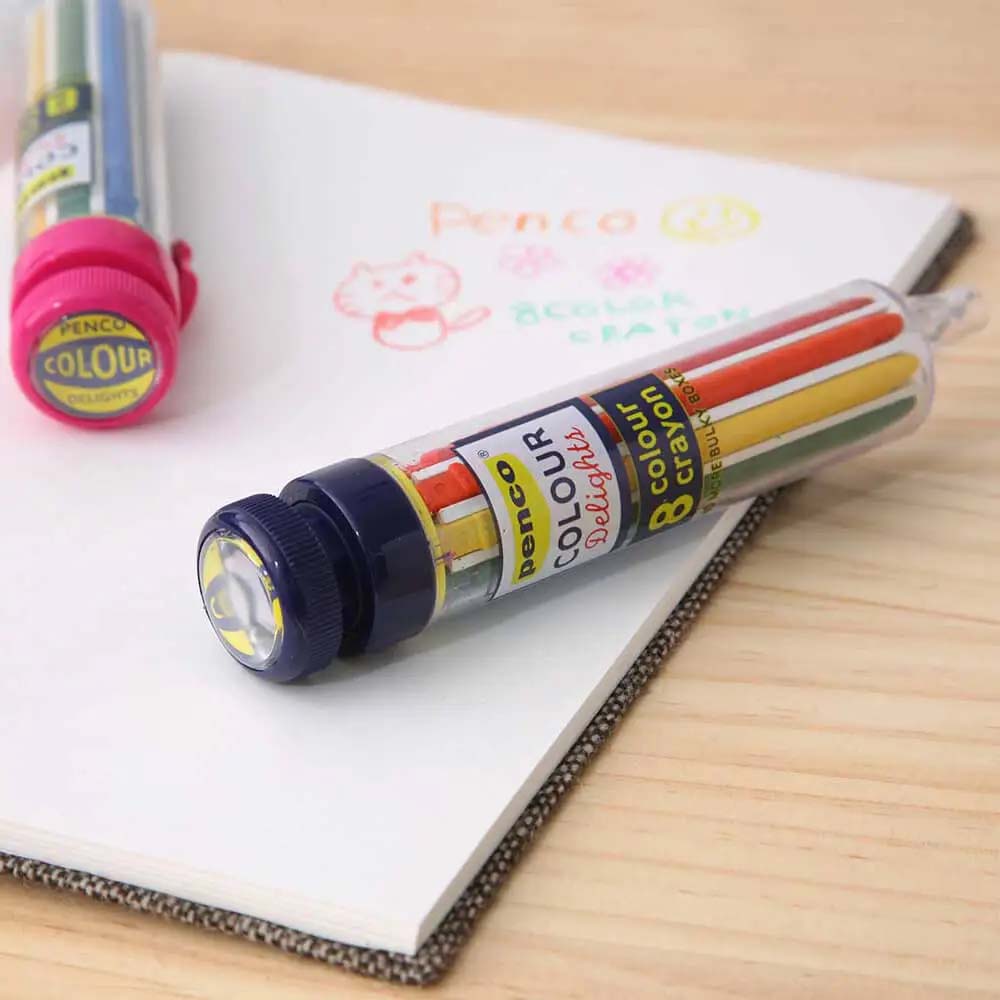 Tube of Benco Colour Delights crayons on a notebook with colorful drawings.