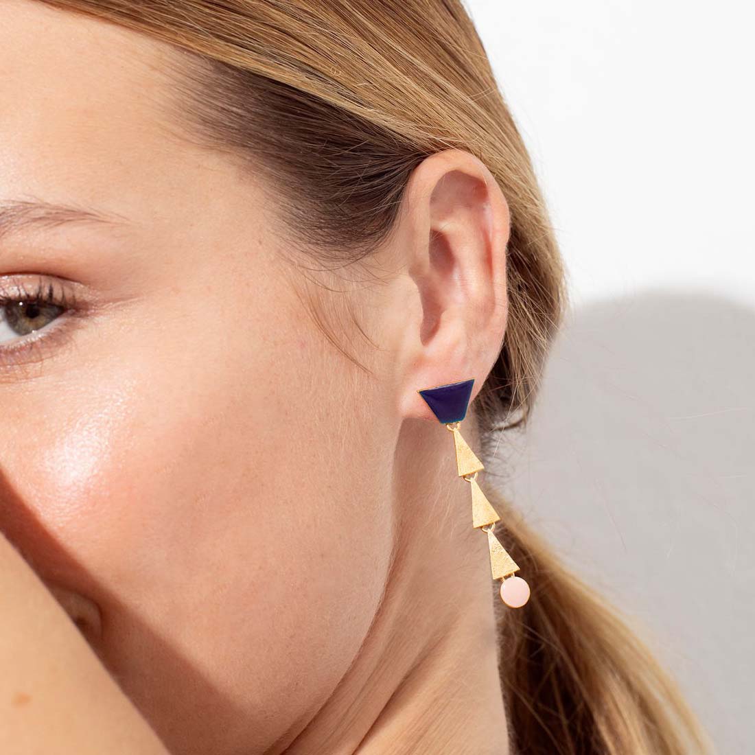 Pair of earrings with blue, gold, and pink geometric shapes on a white background