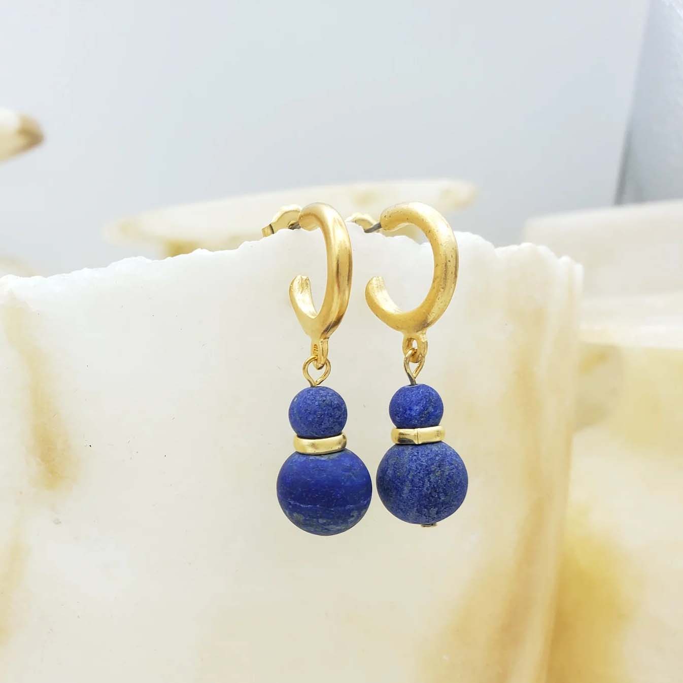 Gold hoop earrings with blue spherical beads on a white background
