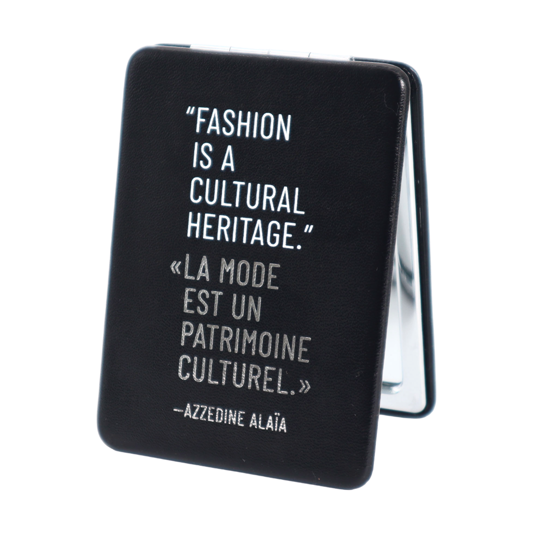 A black folding compact mirror with a white printed quote by Azzedine Aláa on the front, photographed on a clean white background.