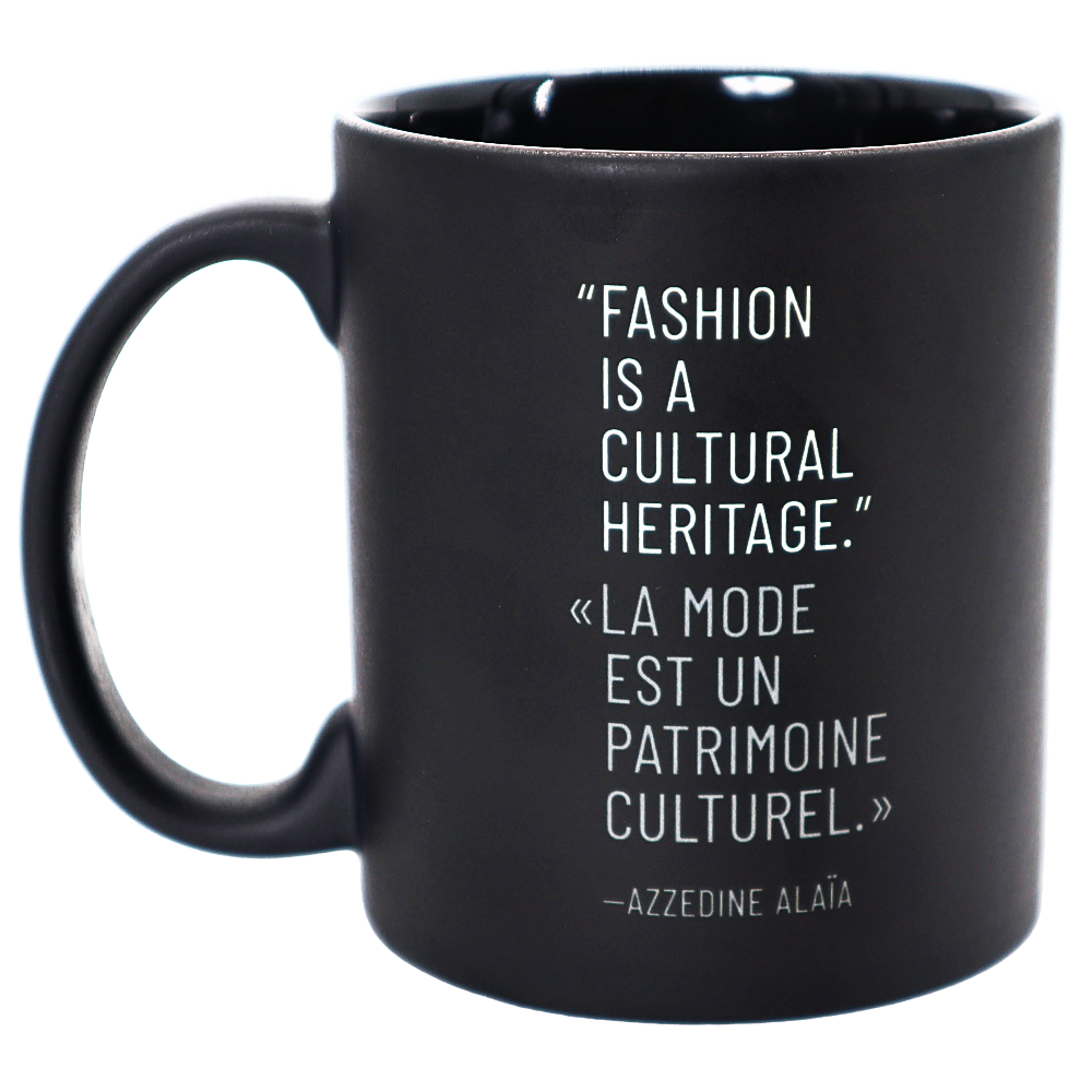 A matte black ceramic mug with a white printed quote by Azzedine Alaéa on the side, shown against a plain white background.
