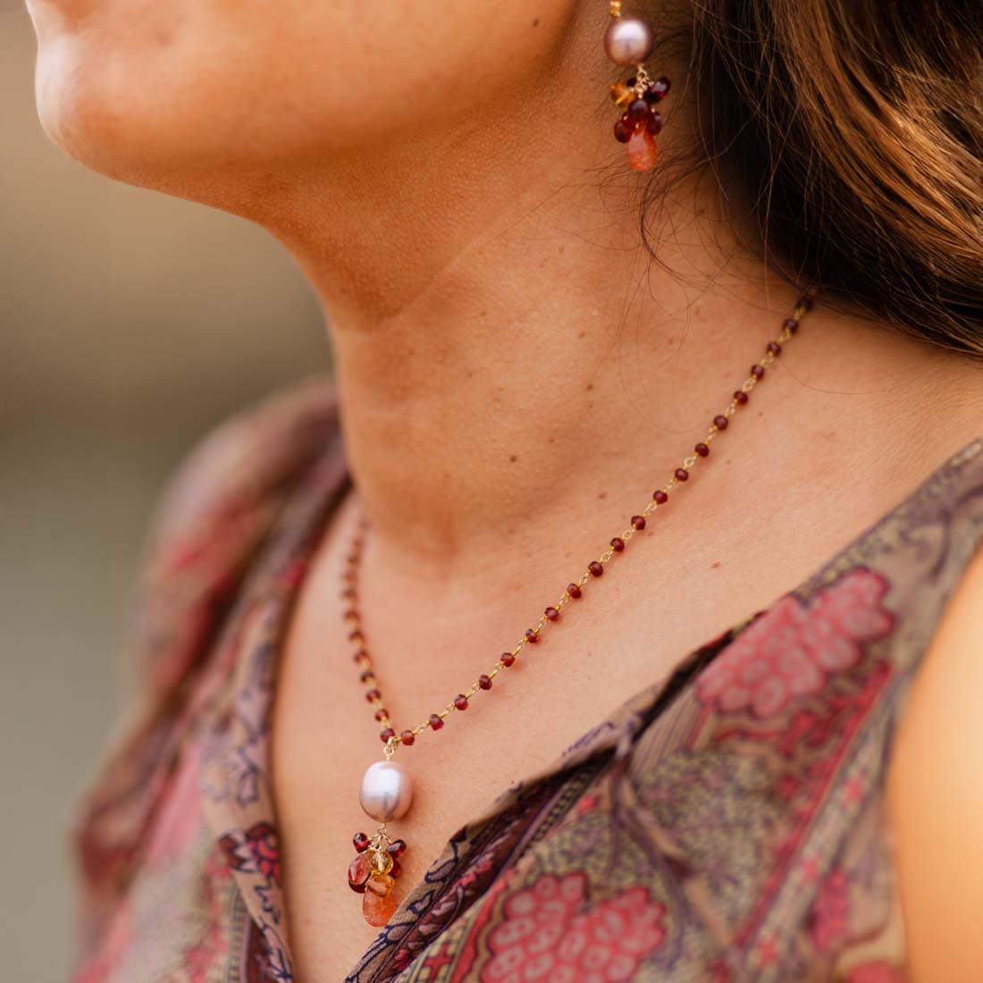A gold-plated chain necklace featuring a champagne Edison pearl pendant with garnet and citrine beads, and a sunstone drop.
