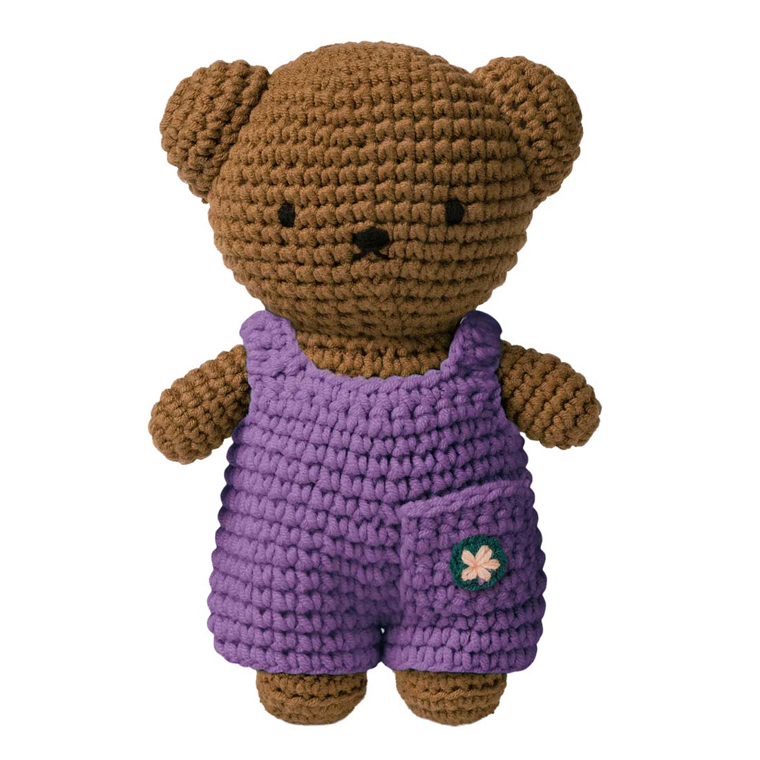Crocheted teddy bear wearing purple overalls on a white background