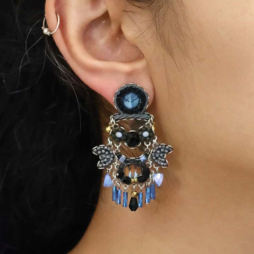 Pair of ornate earrings with blue and black gemstones on a white background