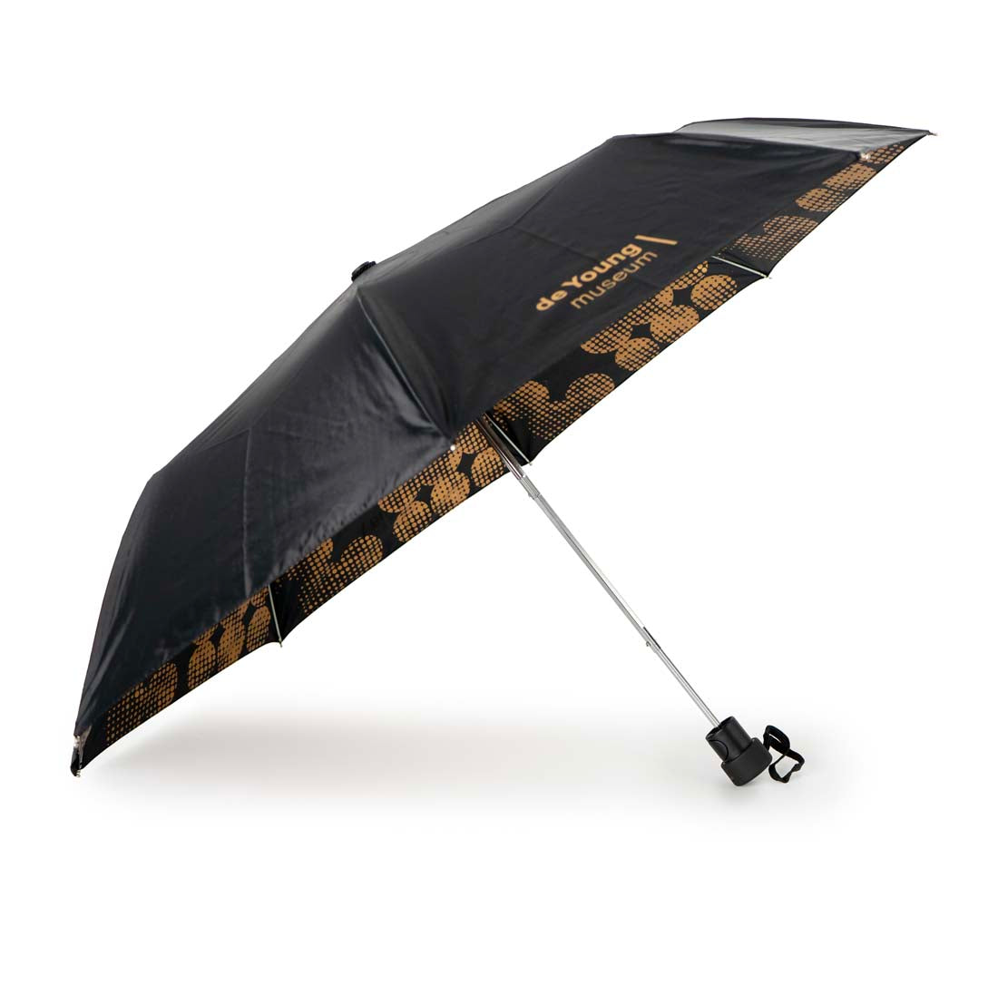 A retractable folding umbrella with a geometric pattern featuring copper dots on the inside, with a black exterior. de Young Copper Dots Folding Umbrella