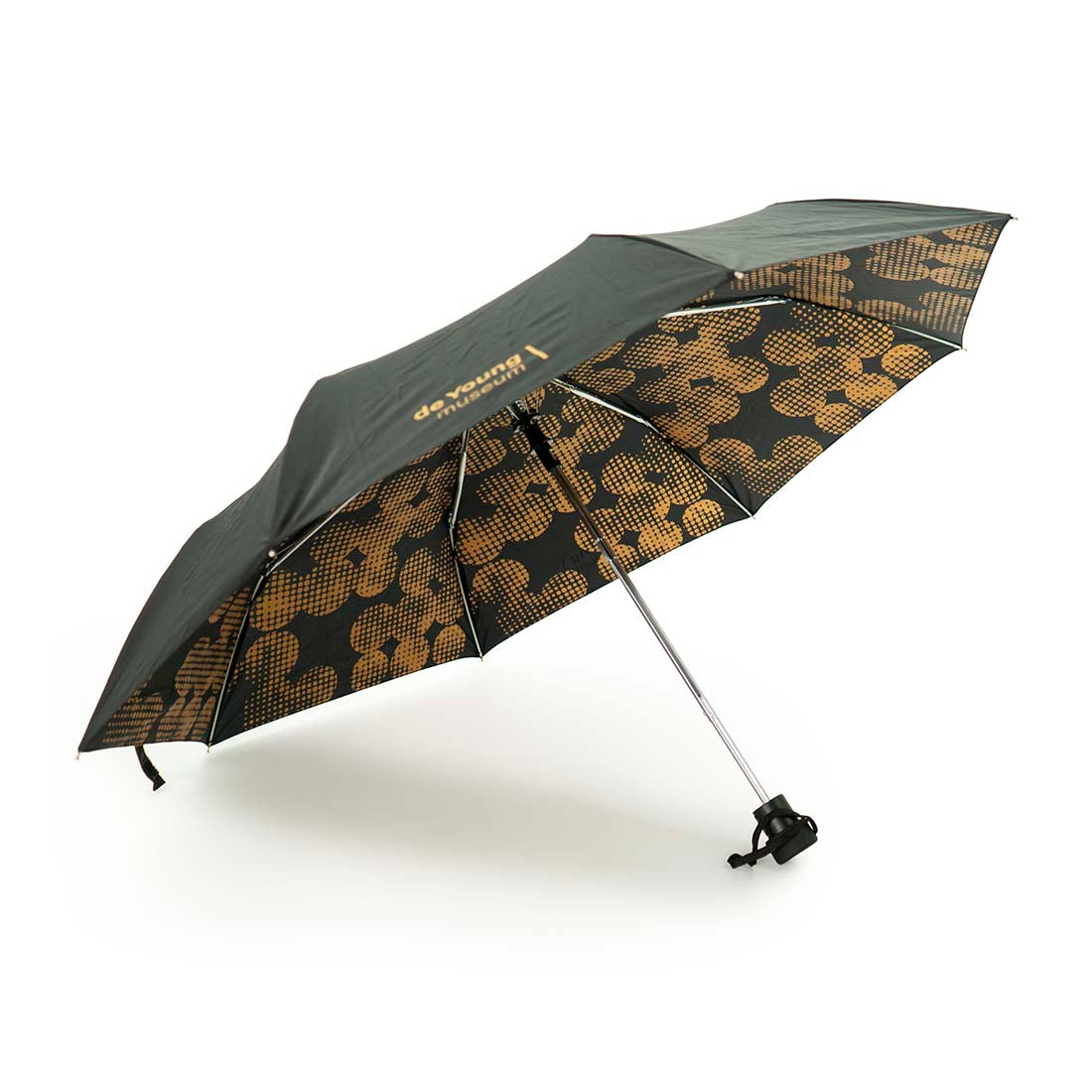 A retractable folding umbrella with a geometric pattern featuring copper dots on the inside, with a black exterior. de Young Copper Dots Folding Umbrella