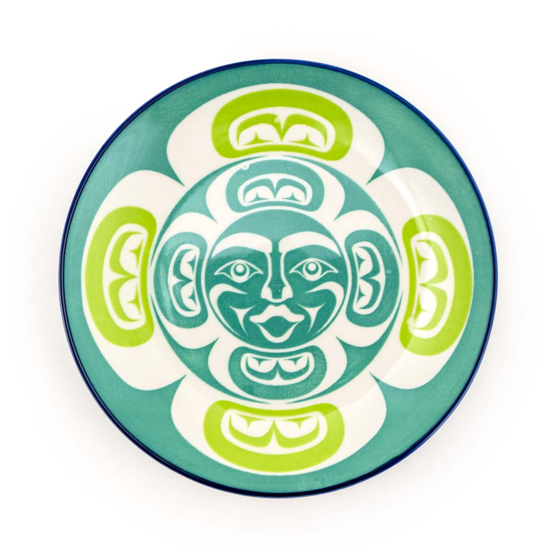 A round porcelain plate with a central Indigenous artistic face design surrounded by green and white geometric patterns with a blue rim.
