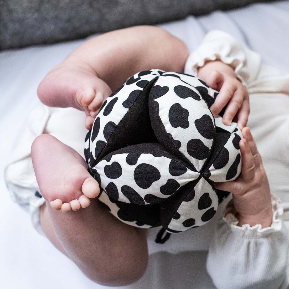 A black and white polka-dotted sensory grasp ball with a hook for hanging.
