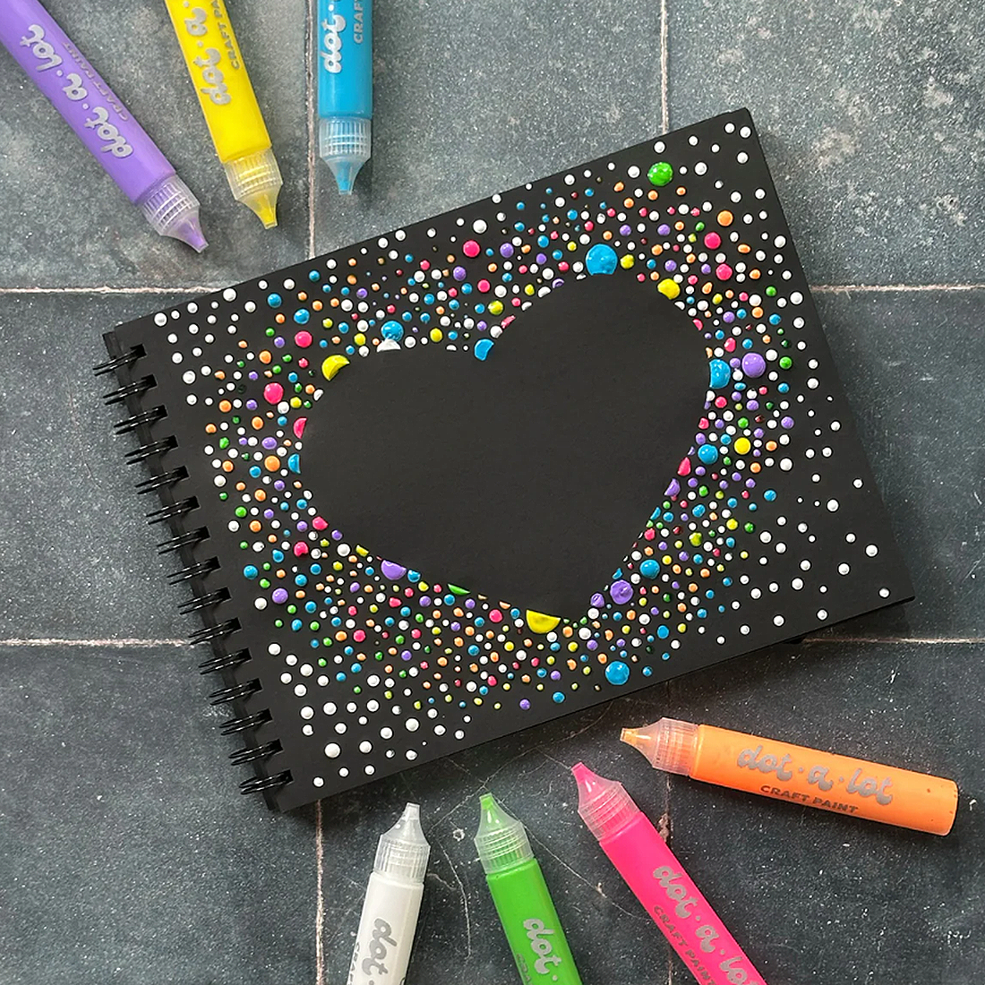 Black notebook with colorful dot pattern on a gray surface with dot markers around