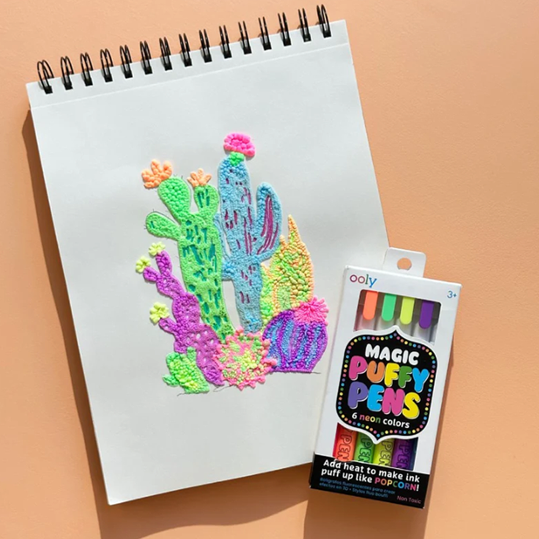 Colorful puffy paint drawing of a cactus on a notebook with Magic Puffy Pens packaging.