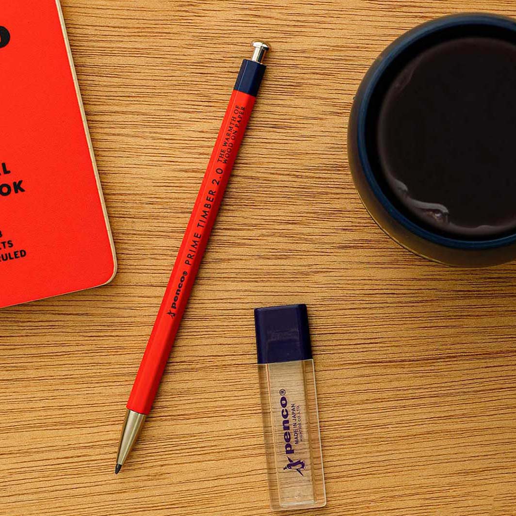Red pen, small bottle, and red notebook on a wooden surface