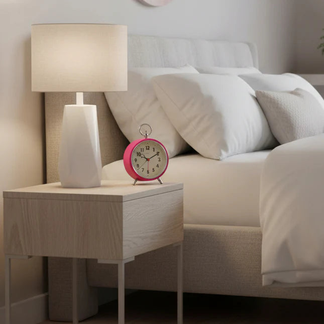Pink alarm clock on a nightstand next to a bed with white pillows