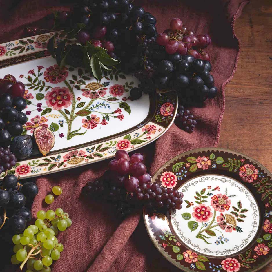 Decorative plates with floral designs surrounded by grapes on a wooden surface.