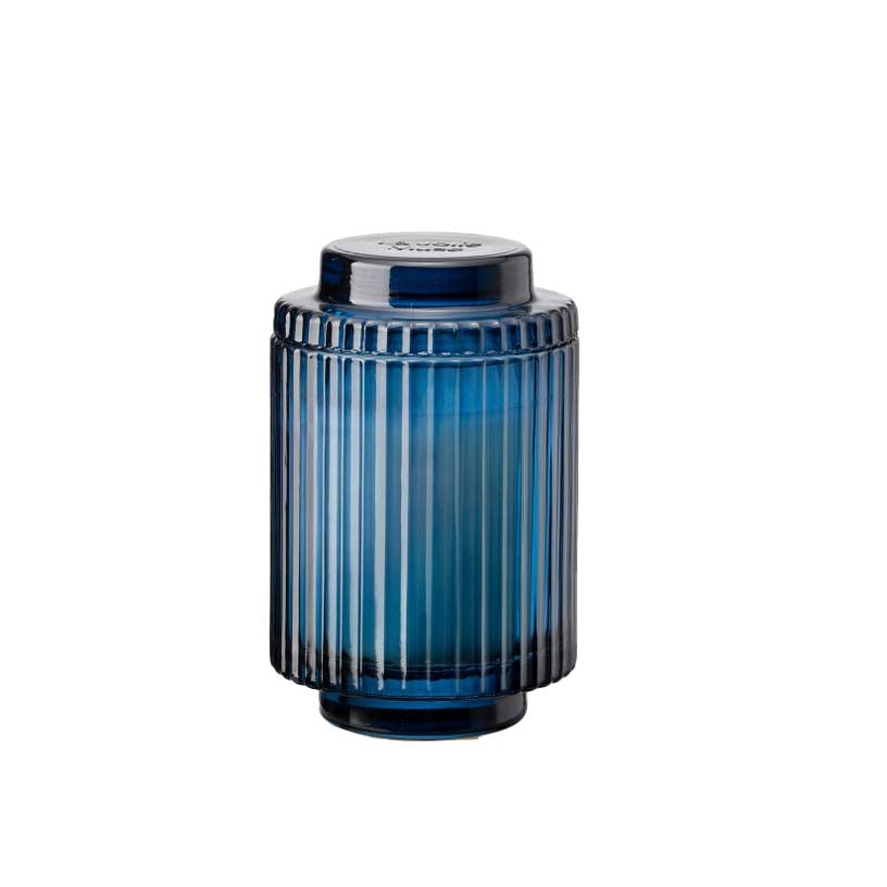 A blue ribbed glass candle holder with a white candle inside, on a white background. Amélie Eucalyptus & Sage Candle