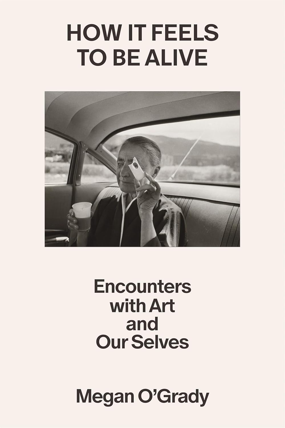 Book cover of 'How It Feels To Be Alive' by Megan O'Grady featuring a black and white photo of a person in a car.