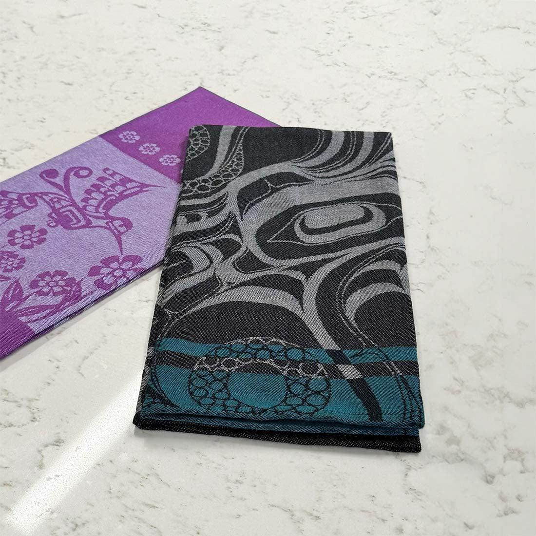 A black cotton tea towel with a white octopus pattern and a teal blue border.