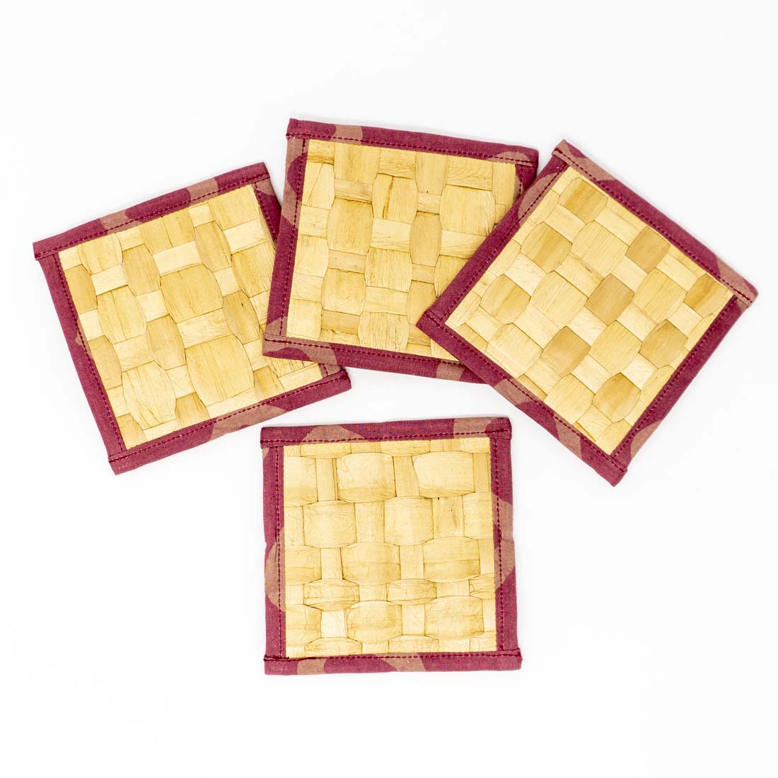 A set of four square coasters made of water hyacinth, with a geometric pattern and red batik edging, tied together with a string.